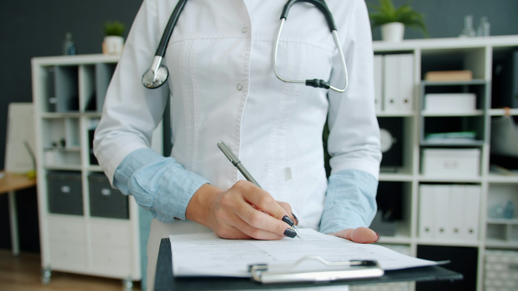 Close-up of a clinician's hand writing in medical records at an office desk