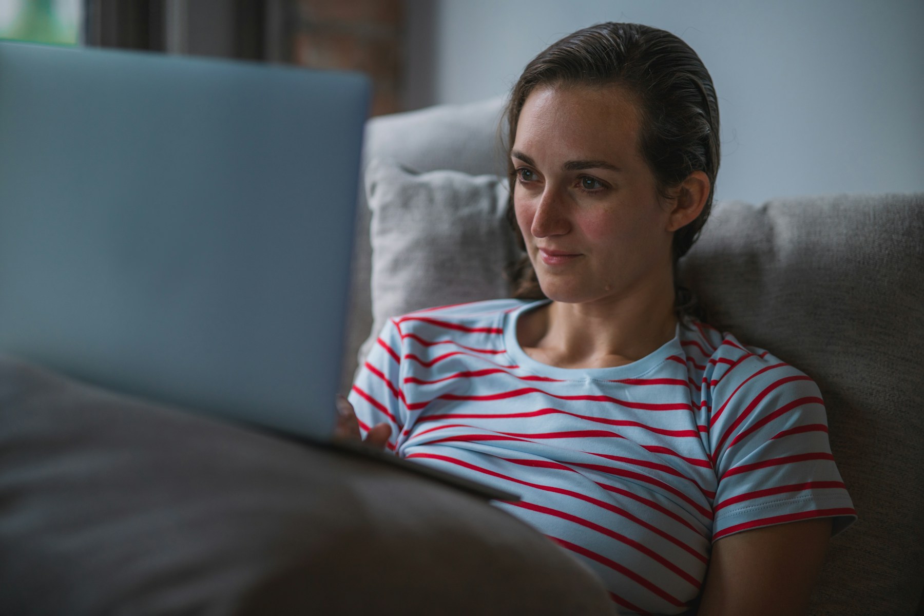 Woman sitting on a couch at home using a laptop to research a question