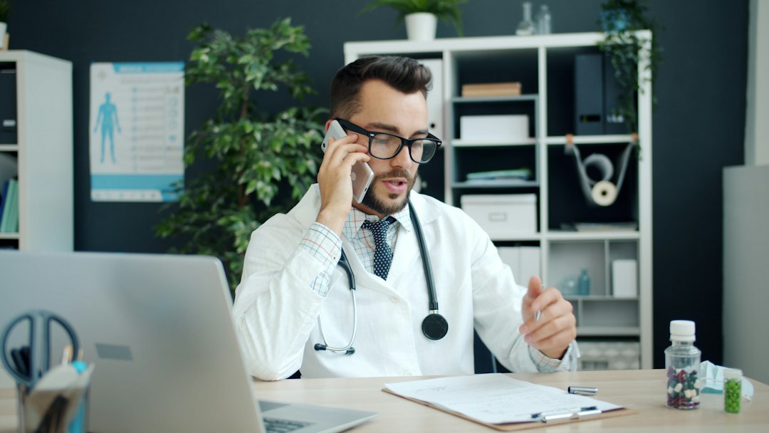 Doctor on the phone with a patient while taking notes at a laptop in a medical office
